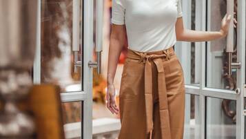 A person standing in front of a glass door with a metal handle, wearing a white top and brown pants.