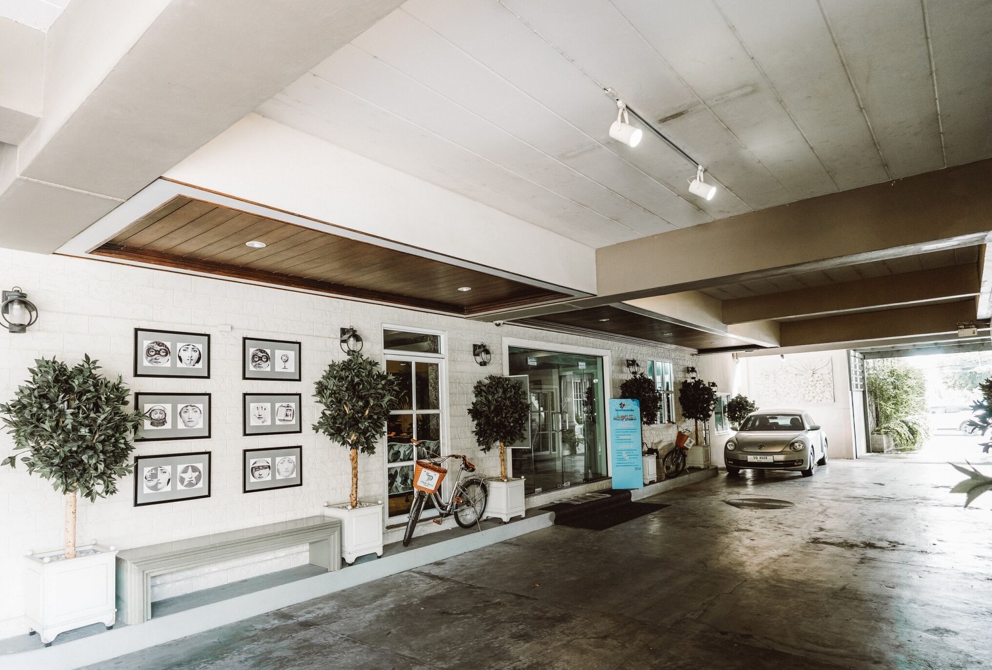 A clean, modern entrance with a white tiled wall, framed artwork, potted plants, and a bicycle.