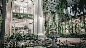 The Club Tree Hotel's exterior with a large arched window, indoor garden with hanging plants, and outdoor seating area. - Club Tree Hotel (Songkhla)