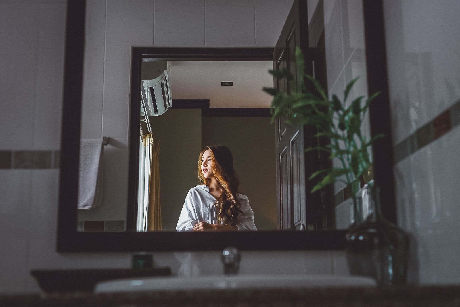 A bathroom with a large mirror, a towel hanging on the wall, and a potted plant.
