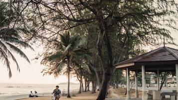 A park with a paved path, a gazebo, and a beach in the background.