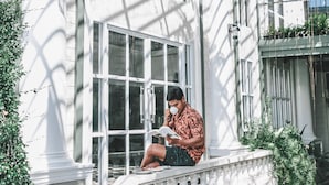 A person sitting on a white balustrade reading a book. - Club Tree Hotel (Songkhla)