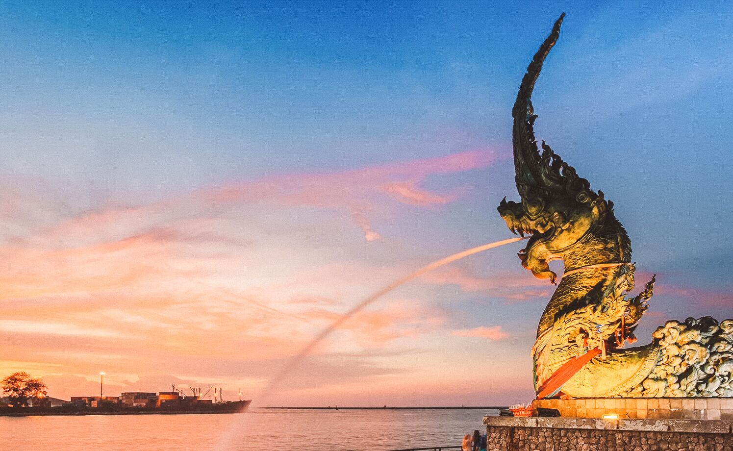 A large dragon statue by the waterfront during sunset.