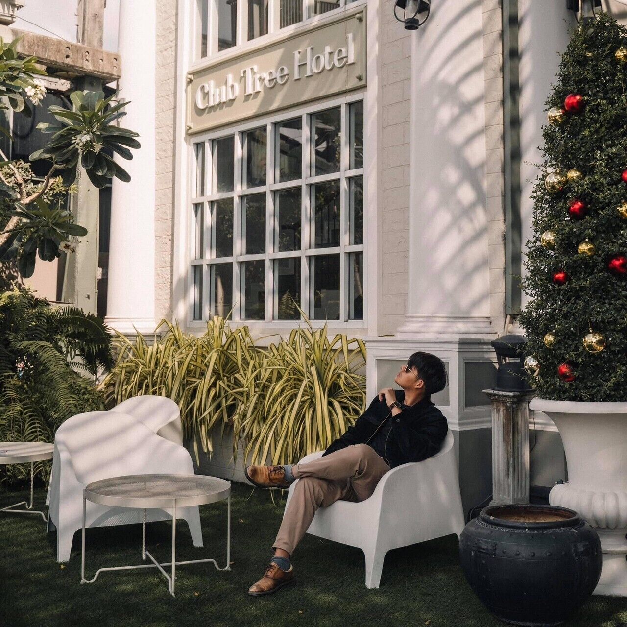 A person sitting on a white outdoor bench in front of a building labeled "Chub Tree Hotel."