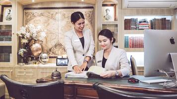 A professional office setting with two individuals at a desk, surrounded by bookshelves, a globe, and a decorative world map.