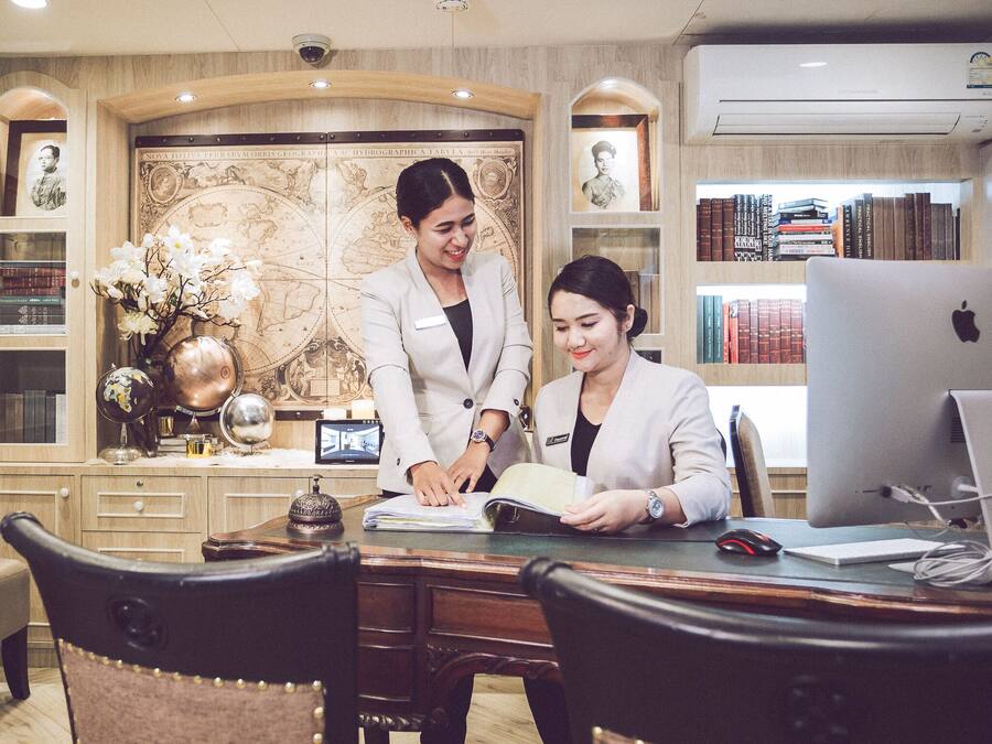 A professional office setting with two individuals at a desk, surrounded by bookshelves, a globe, and a decorative world map.