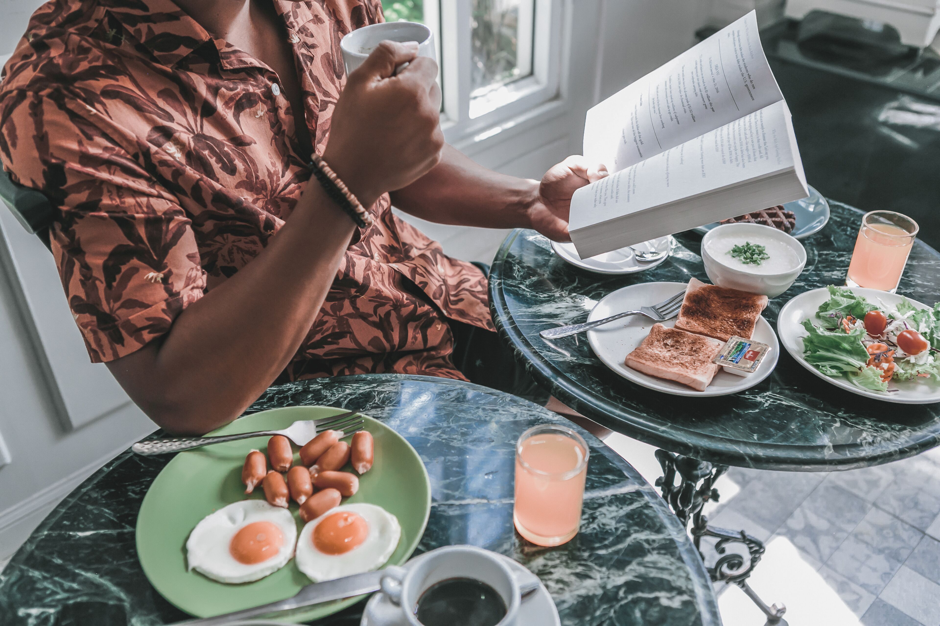 A person reading a menu at a table with breakfast items including eggs, sausages, toast, and a salad.