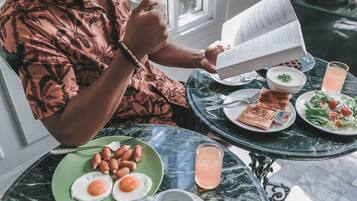 A person reading a menu at a table with breakfast items including eggs, sausages, toast, and a salad.