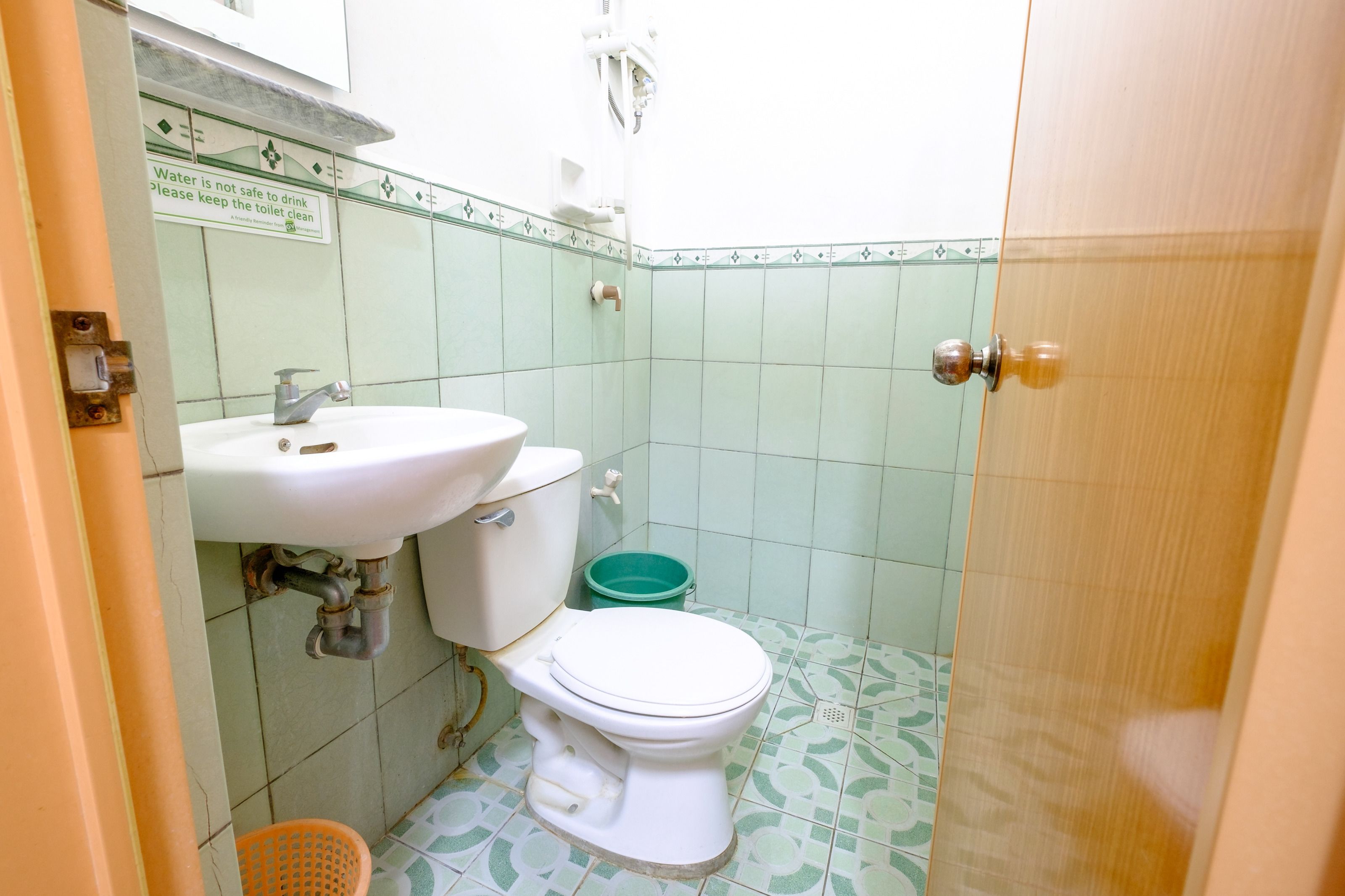 Ein kleines Badezimmer mit Toilette, Waschbecken und Fliesen mit grünem Muster.