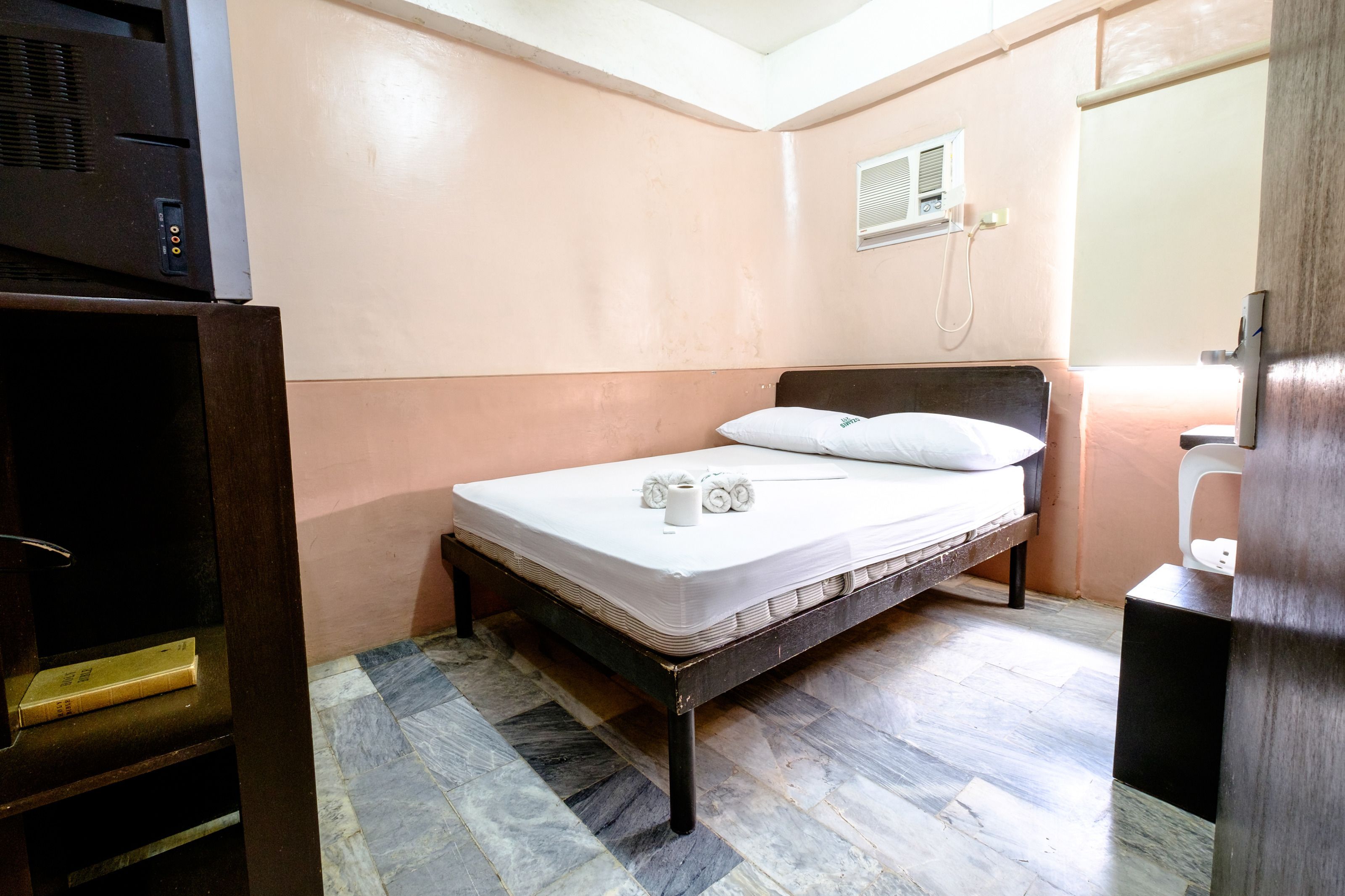 A small, single-bed room with a wooden headboard, a bedside table, and a built-in heater.