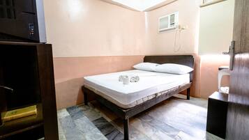 A small, single-bed room with a wooden headboard, a bedside table, and a built-in heater.