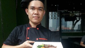 Una persona con uniforme de chef negro sostiene un plato con comida.