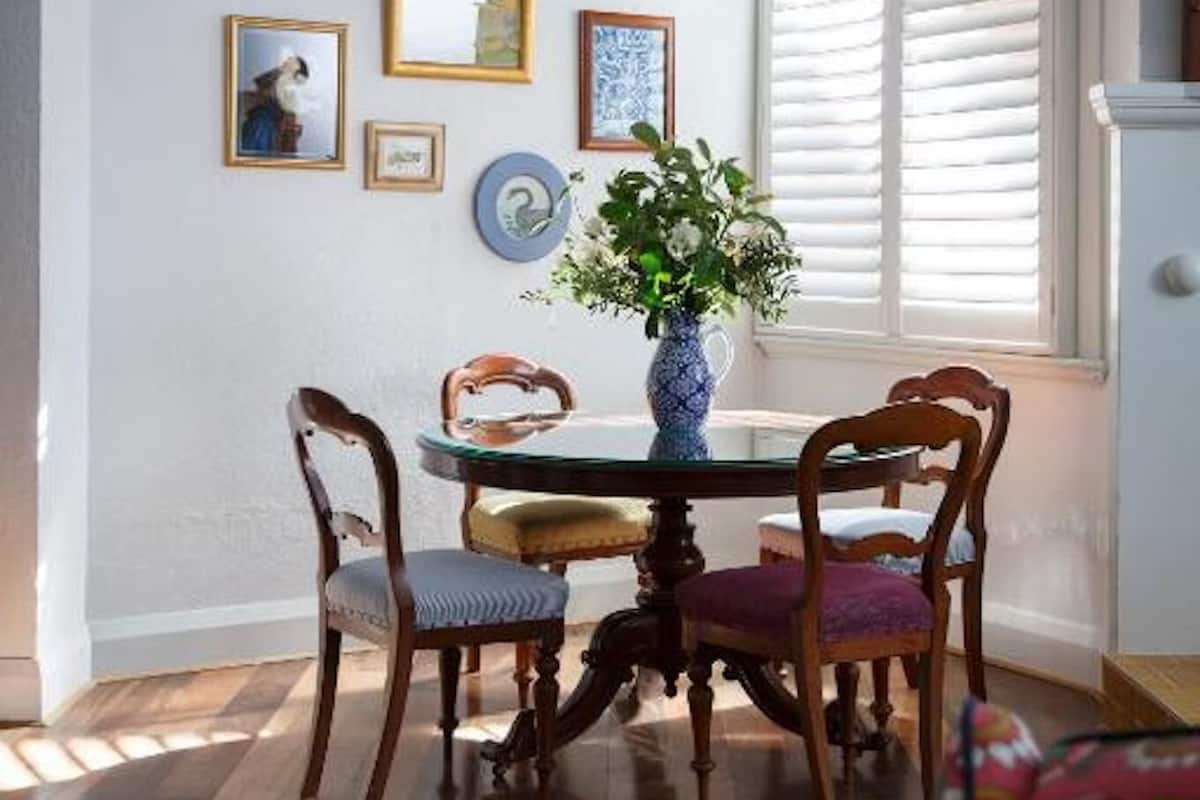 Un comedor con una mesa de madera, cuatro sillas y un florero con flores. En la pared hay cuadros enmarcados.