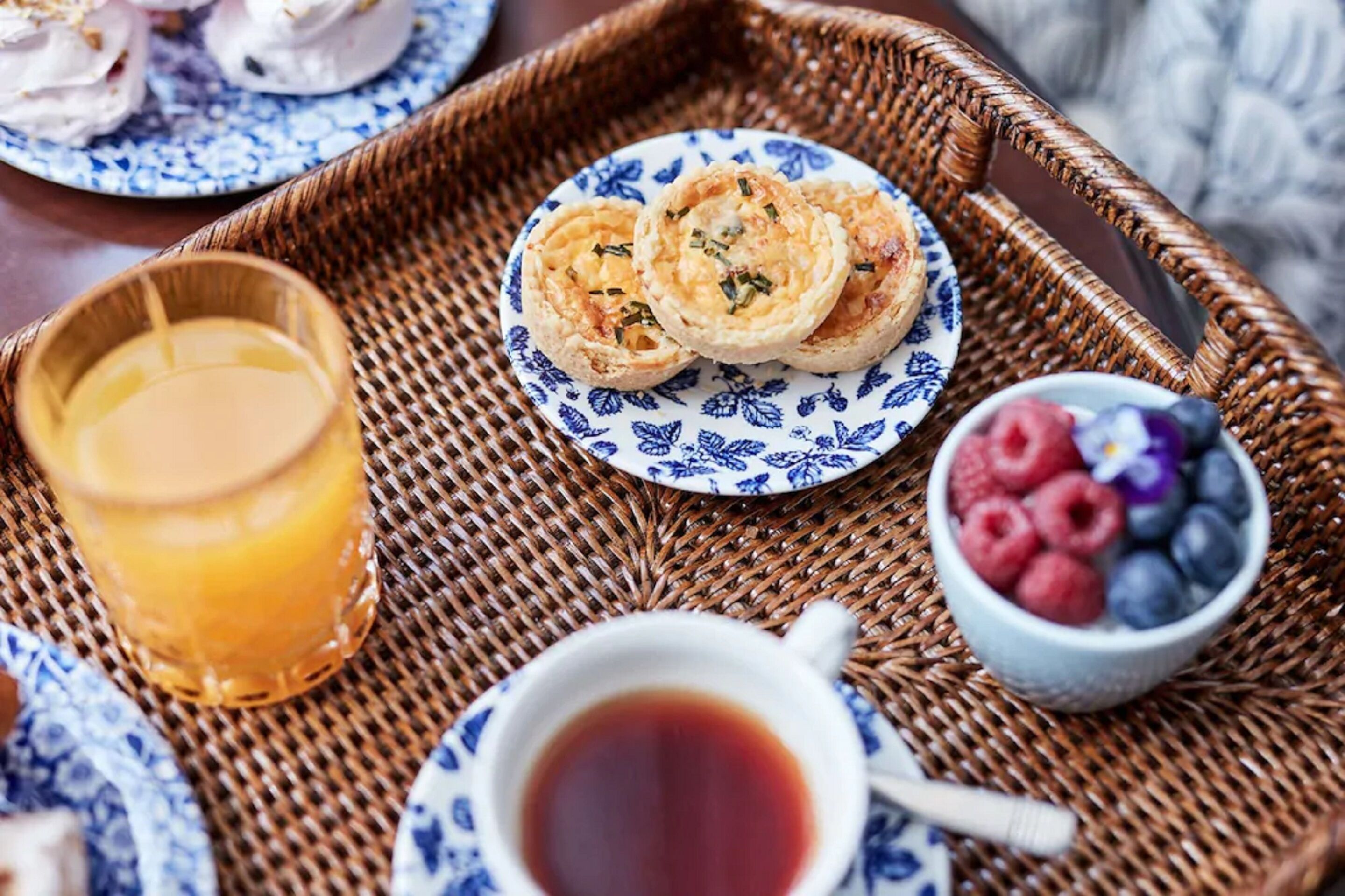 A breakfast tray with pastries, a glass of orange juice, a cup of tea, and a bowl of berries.