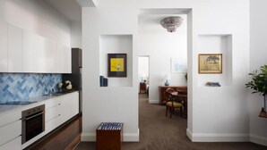 A modern kitchen with white cabinets, a blue herringbone backsplash, and a wooden countertop. There is a dining area with a wooden table and chairs, and a hallway leading to another room. - The Provincial Boutique Hotel (Ballarat)