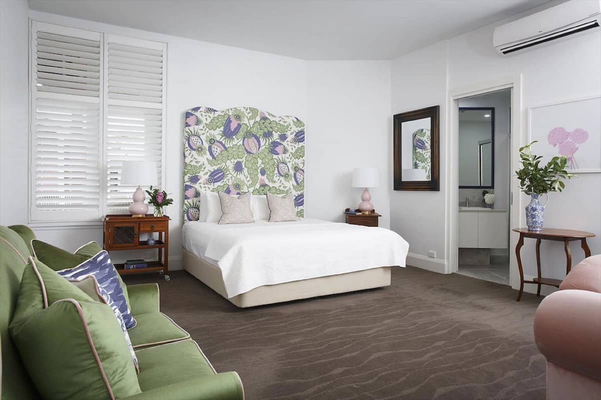 Un dormitorio con cama, sofá verde y un gran cabecero estampado con motivos florales.