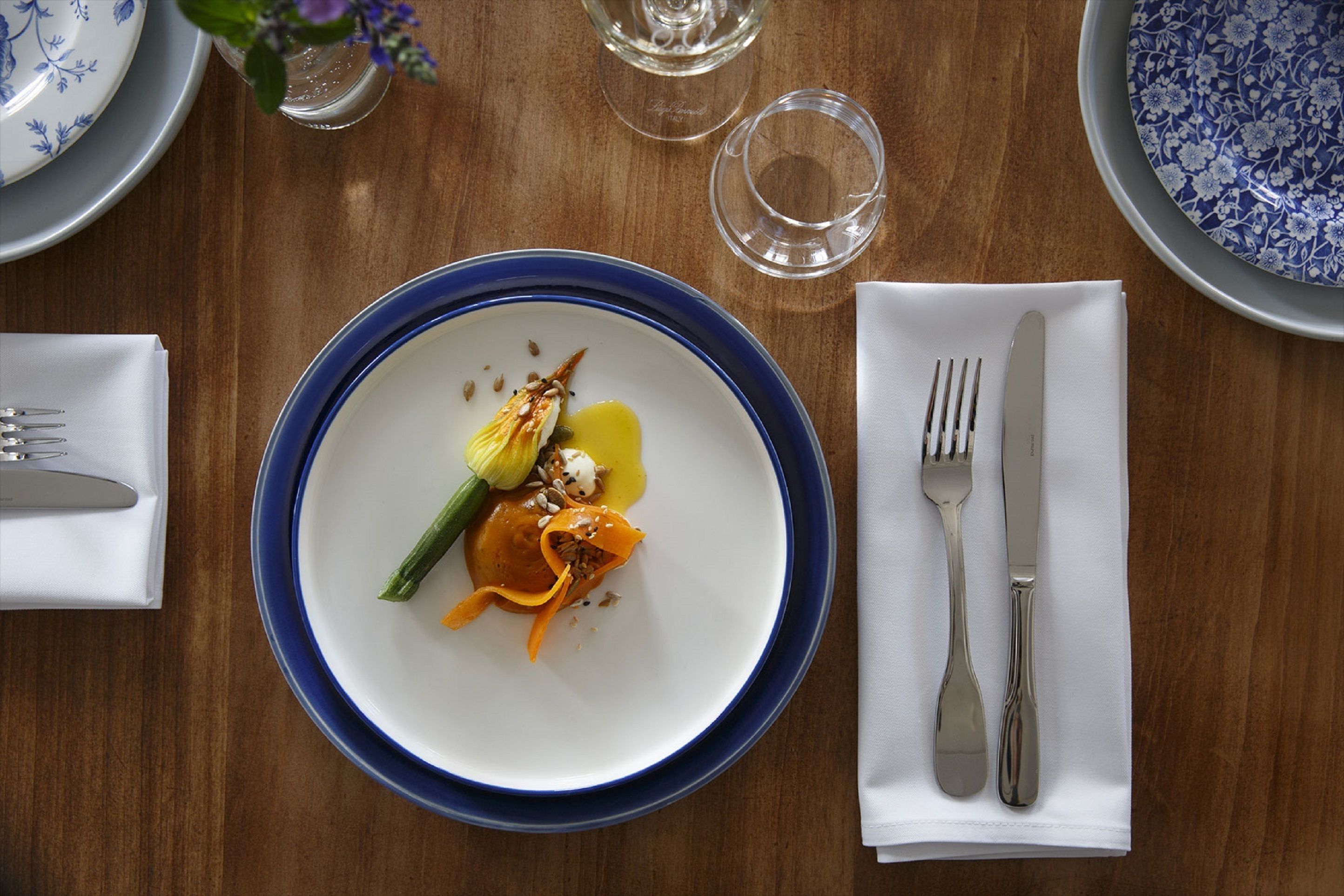 A dining table with a blue-rimmed plate, a fork, and a knife on a white napkin.