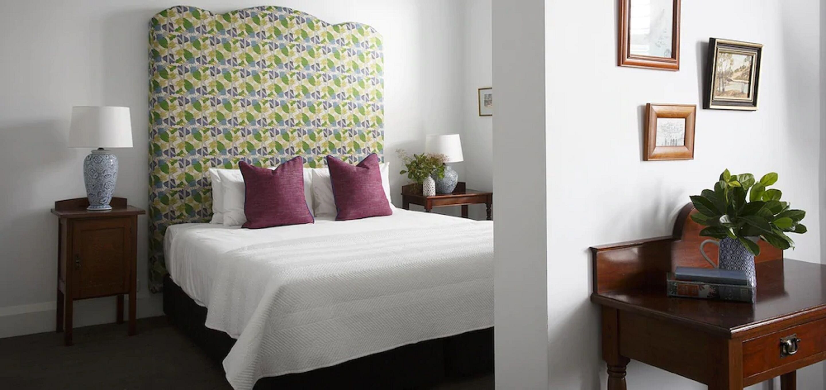 A neatly made bed with a patterned headboard, two bedside tables with lamps, and a small bedside plant.