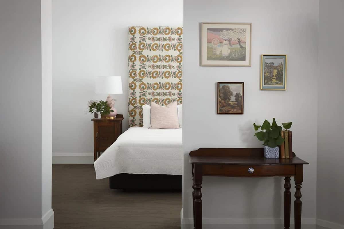 Un dormitorio con una cama, una mesita de noche, una mesilla con una planta y cuadros en la pared.