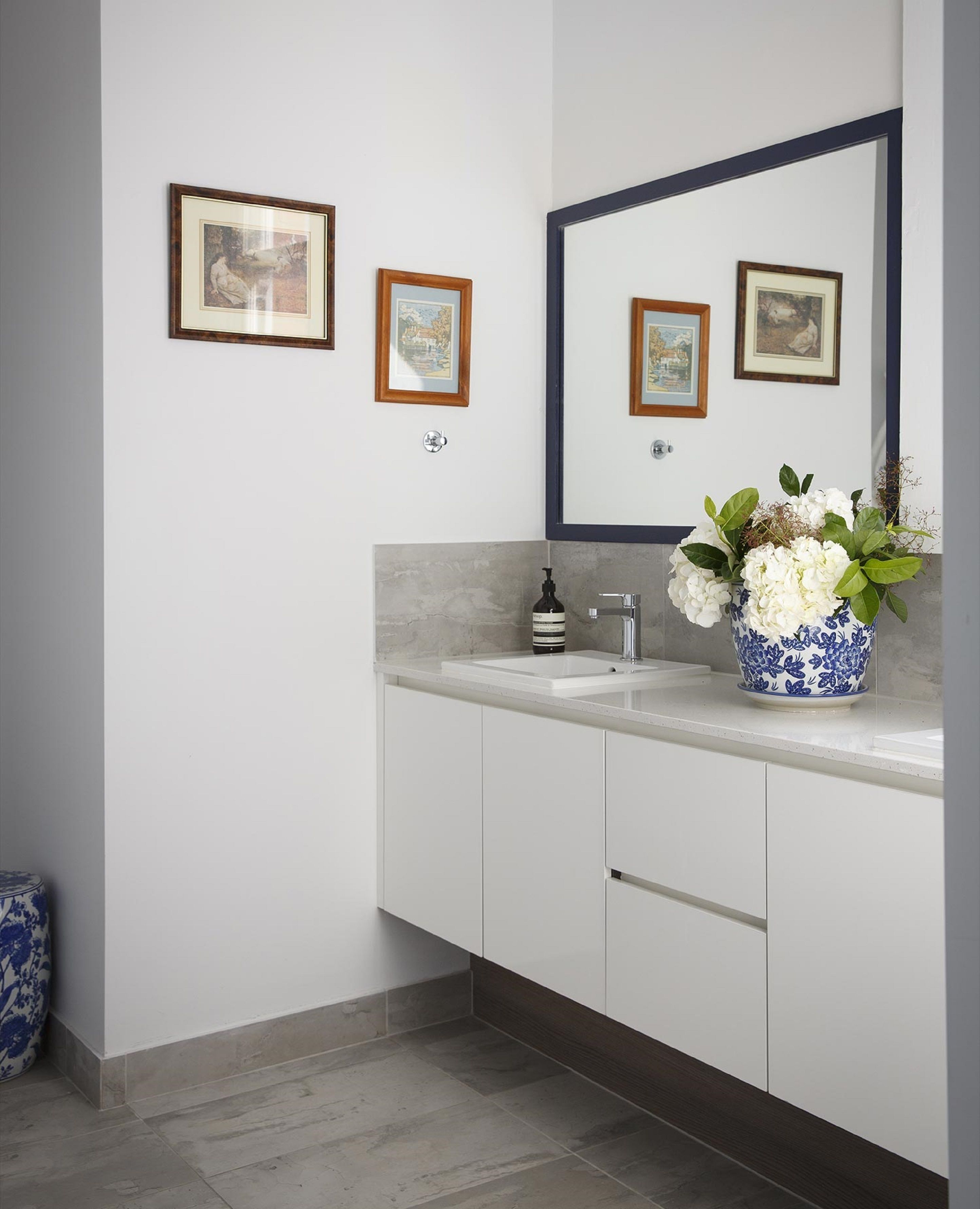 A modern bathroom with a white vanity, a large mirror, and framed artwork on the wall.