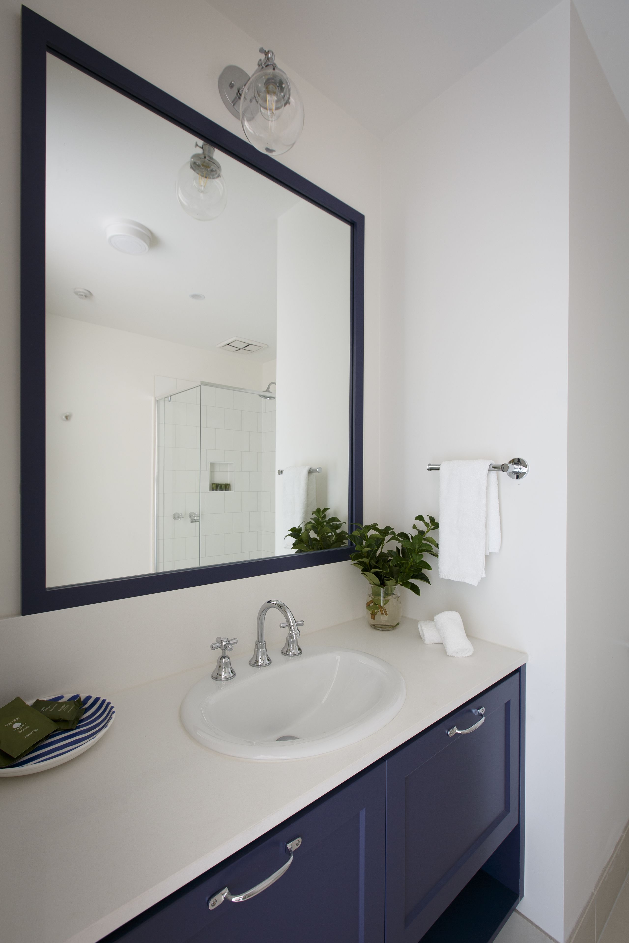 Un bagno con uno specchio grande, un lavandino bianco, un armadietto blu scuro e un porta asciugamani.