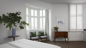 A bedroom with a bed, two chairs, a small table with a vase, a cabinet, and a window with curtains. - The Provincial Boutique Hotel (Ballarat)