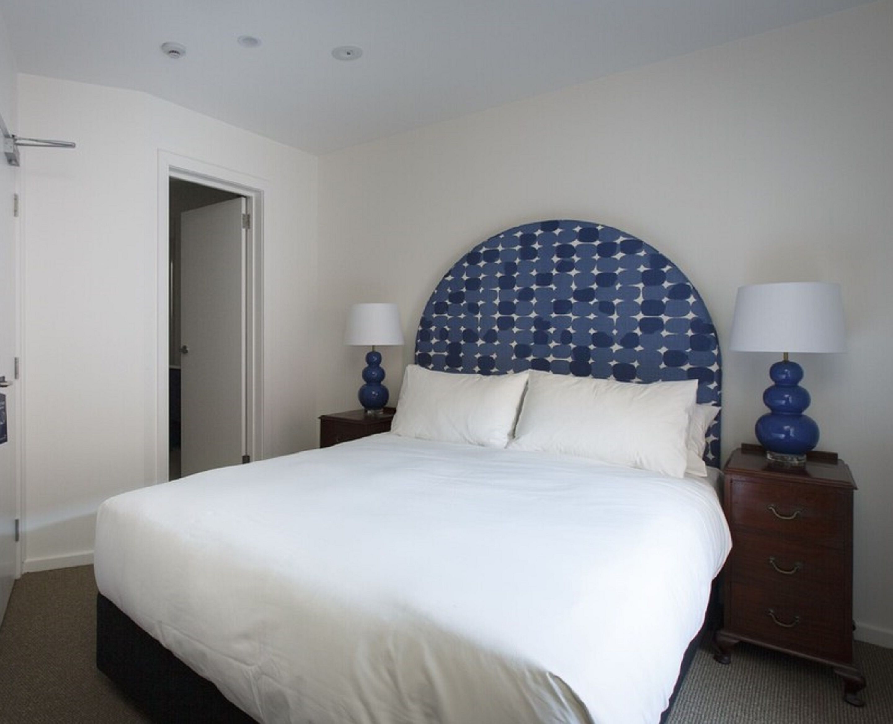 A neatly made bed with a white comforter and pillows, a headboard with a star pattern, two bedside tables with lamps, and a wooden nightstand.