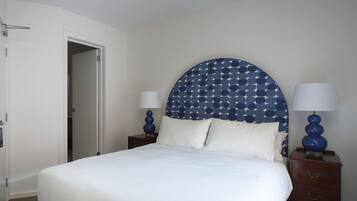 A neatly made bed with a white comforter and pillows, a headboard with a star pattern, two bedside tables with lamps, and a wooden nightstand.