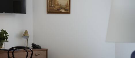 A hotel room with a bed, desk, chair, lamp, and a painting on the wall.