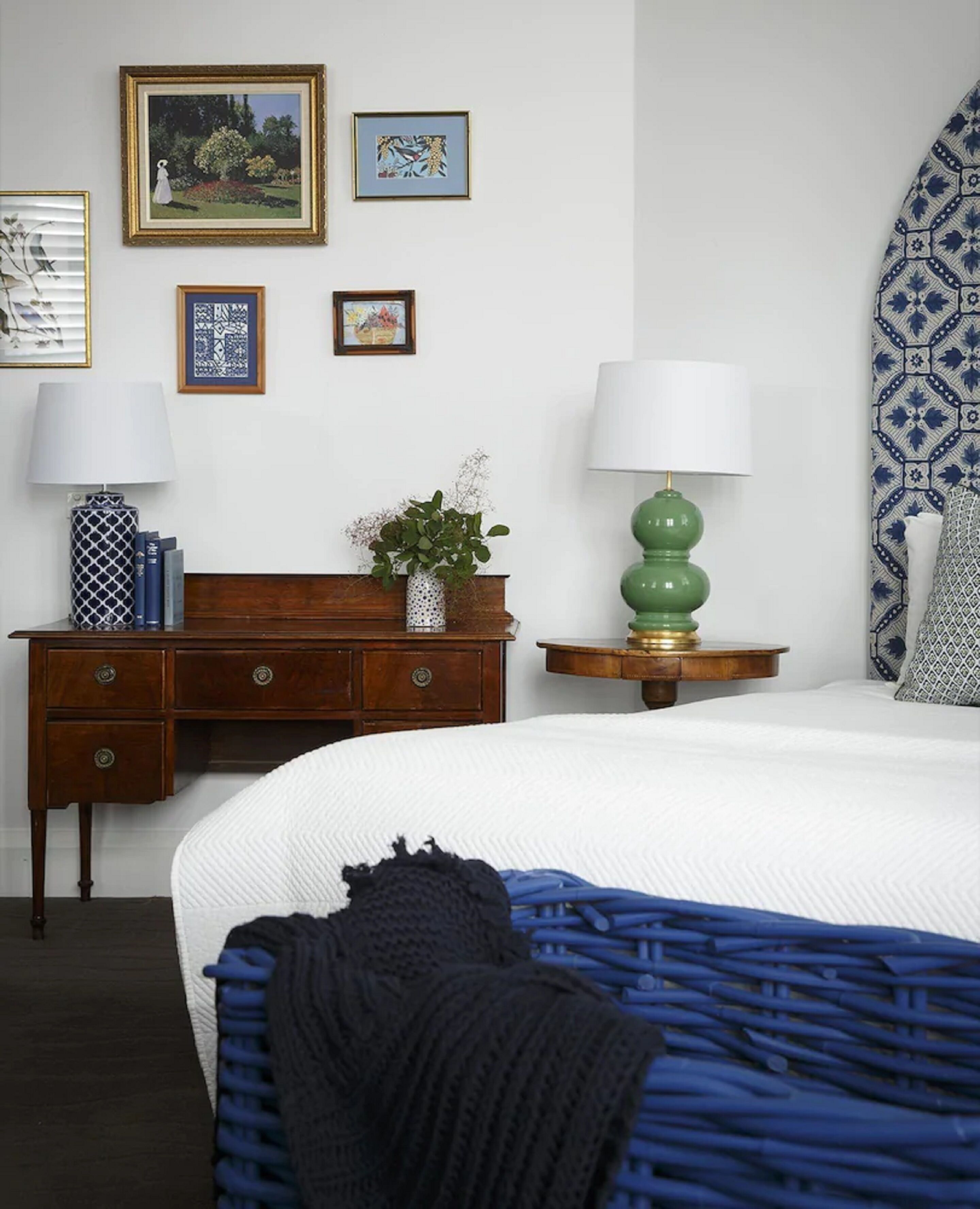 A bedroom with a bed, a wooden dresser, two lamps, and framed artwork on the wall.
