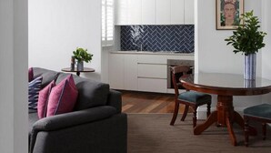 A modern kitchen with white cabinets, a blue patterned backsplash, and a round wooden dining table with chairs. - The Provincial Boutique Hotel (Ballarat)