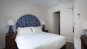 A neatly made bed with a white comforter and pillows, a blue star-patterned headboard, two bedside tables with lamps, and a door leading to another room.
