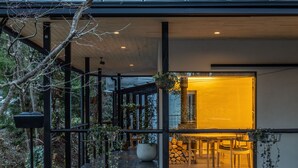 Un edificio moderno con un área exterior cubierta, un espacio de comedor con sillas y una maceta grande.