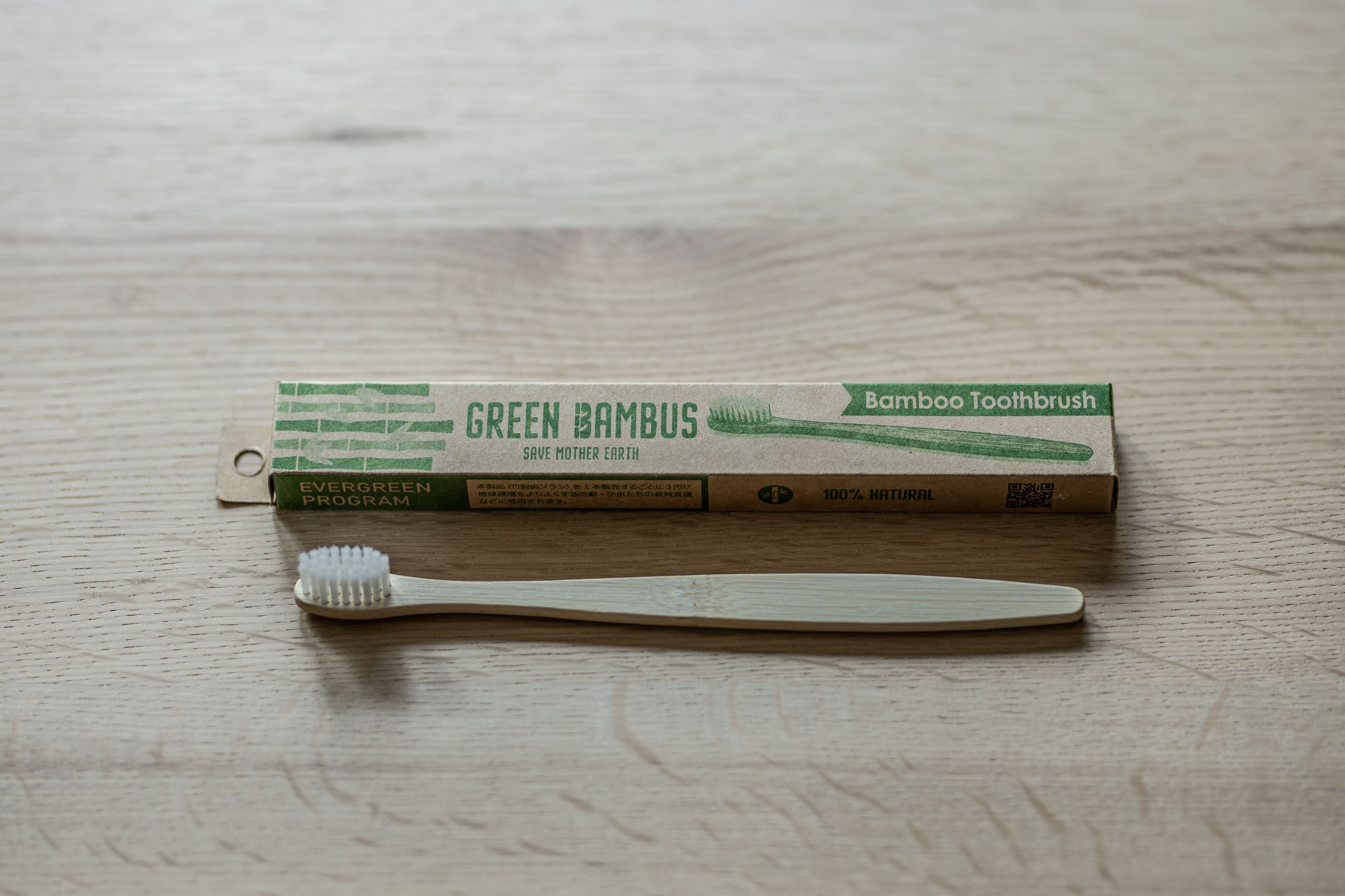 Un cepillo de dientes de bambú y su embalaje sobre una superficie de madera.