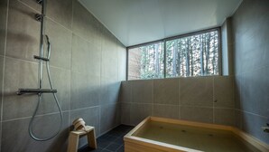 Un baño moderno con una bañera grande, ducha y ventana con vistas a árboles.
