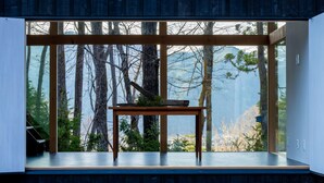 Un interior moderno con un ventanal grande, una mesa de madera y vistas a árboles y montañas.