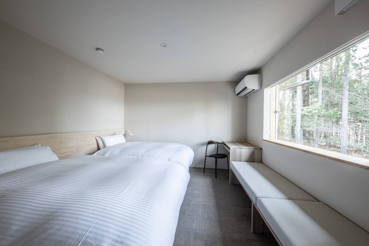Una habitación de hotel moderna con una cama grande, un banco y una ventana con vistas a árboles.