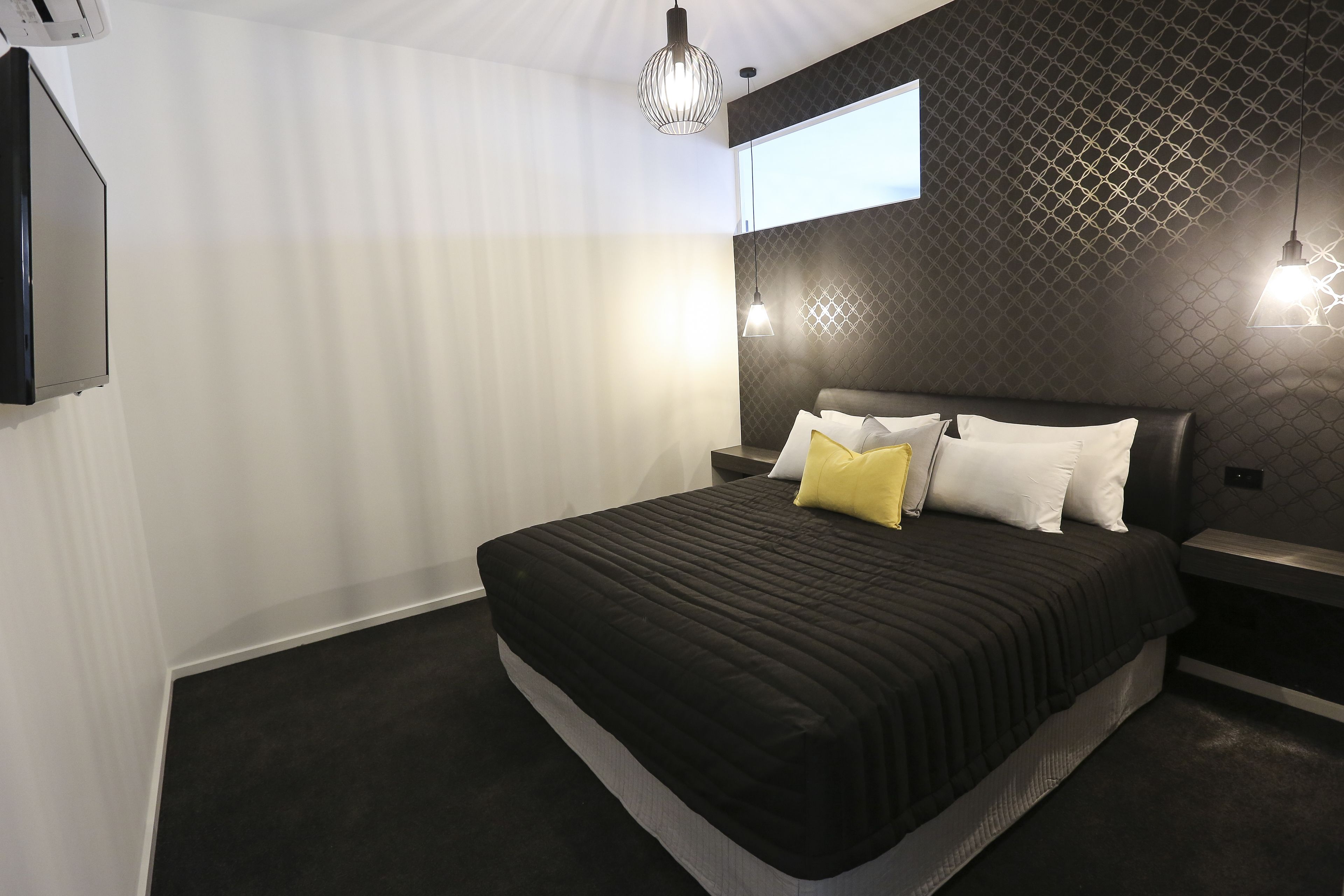 Quarto moderno com uma cama grande, televisão montada na parede e papel de parede com padrão geométrico.