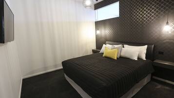 Quarto moderno com uma cama grande, televisão montada na parede e papel de parede com padrão geométrico.