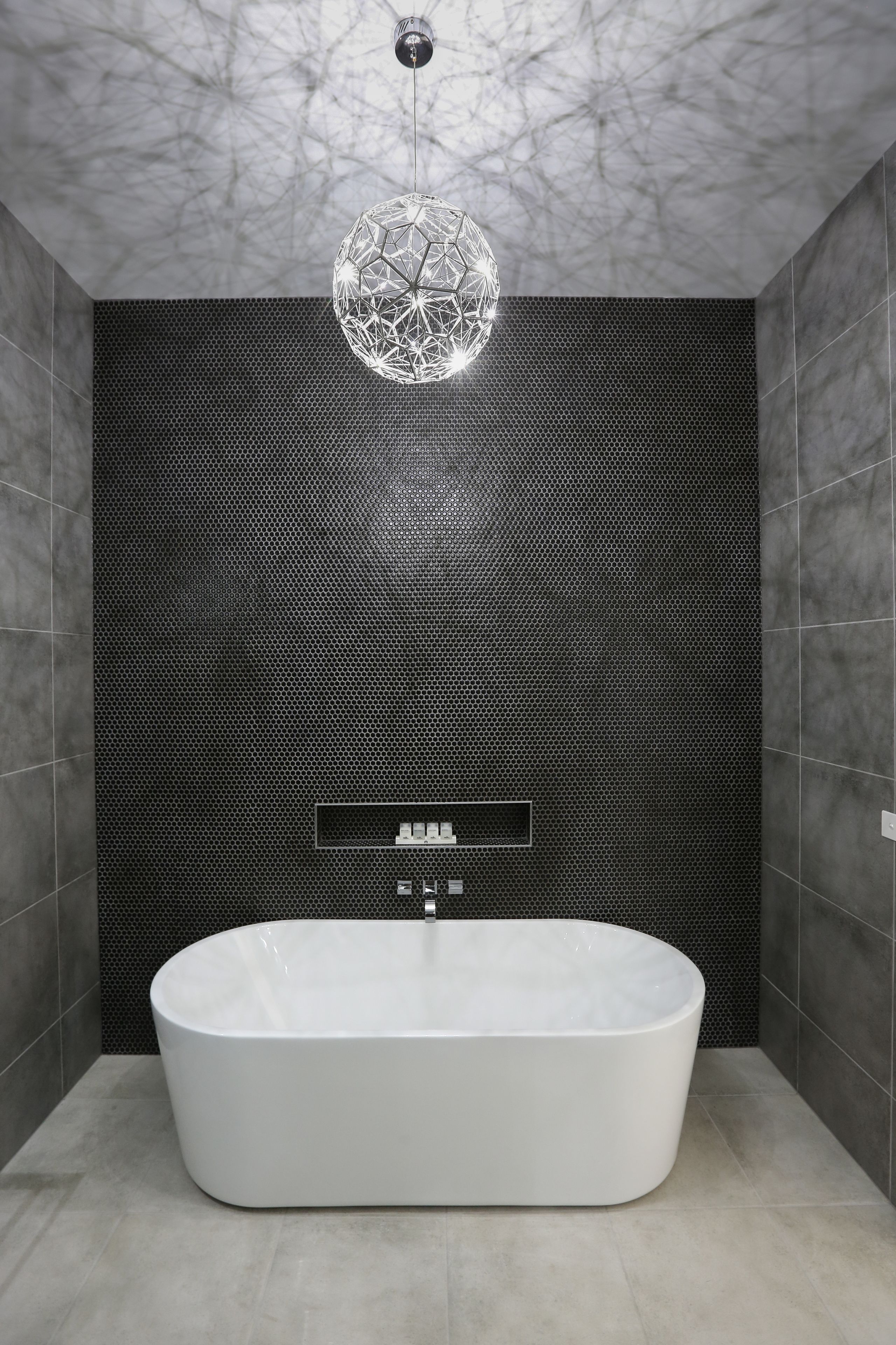 Un bagno moderno con una vasca freestanding, una lampada a sospensione geometrica e un muro testurizzato.