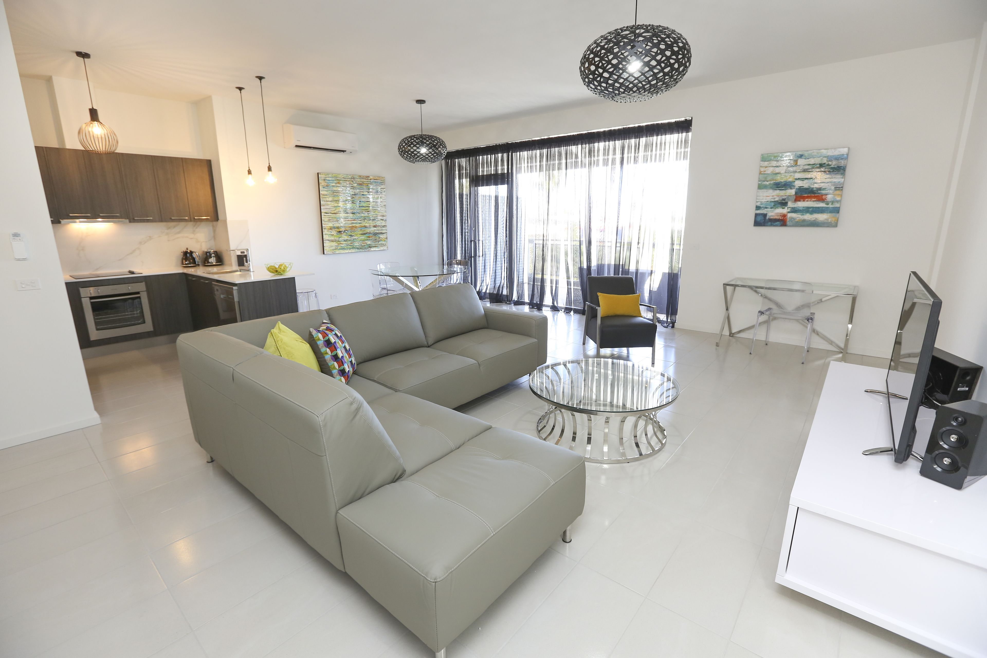 A modern living room with a grey sectional sofa, a glass coffee table, and a white entertainment unit.