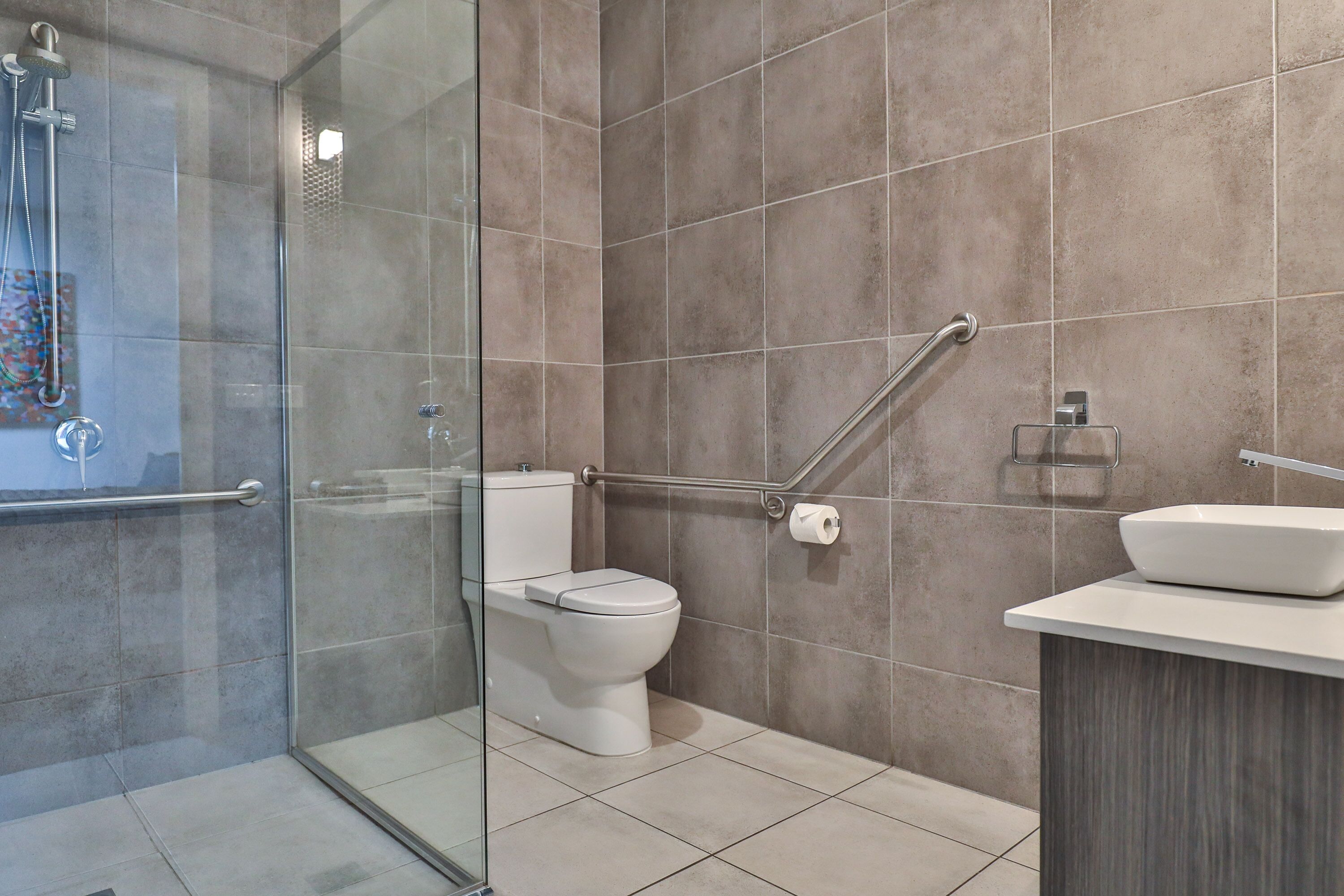Un baño moderno con cabina de ducha de vidrio, inodoro blanco y lavamanos sobre encimera.