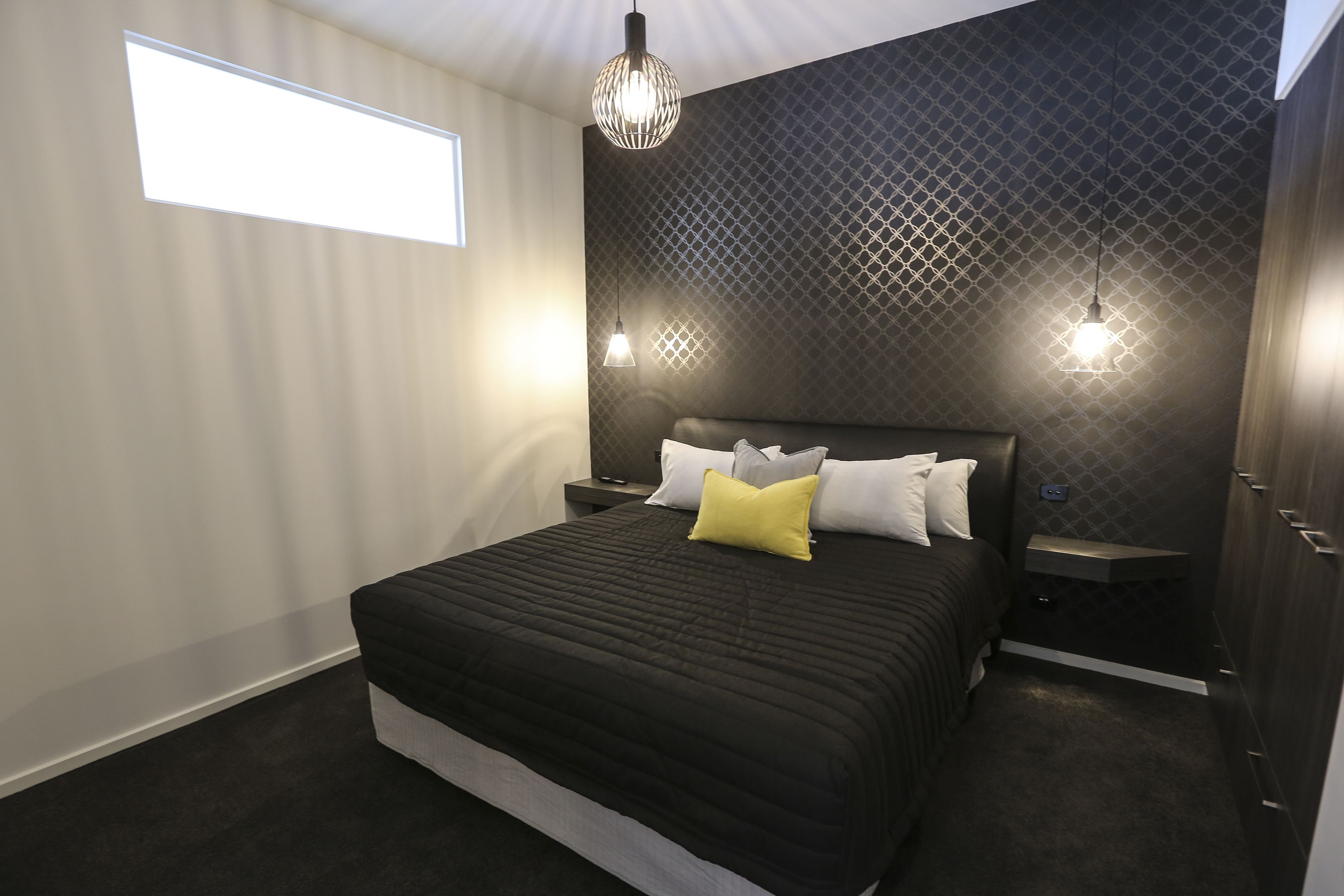 Een moderne slaapkamer met een groot bed, twee nachtkastjes, een hanglamp en een raam dat natuurlijk licht binnenlaat.