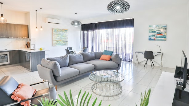 Una sala de estar moderna con un sofá seccional gris, una mesa de centro de vidrio y una zona de comedor con una silla negra.