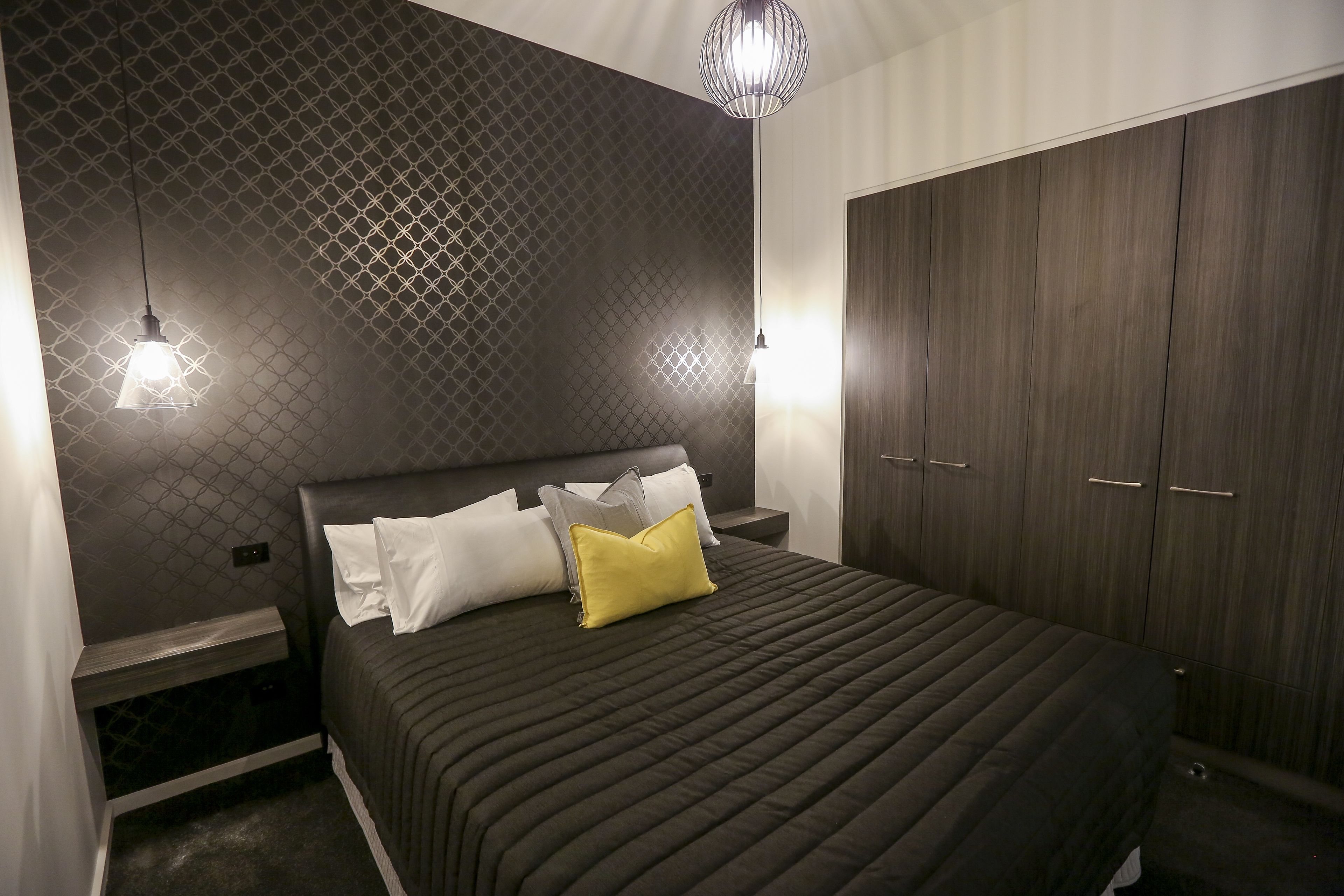 A modern bedroom with a bed, nightstands, and a wardrobe.