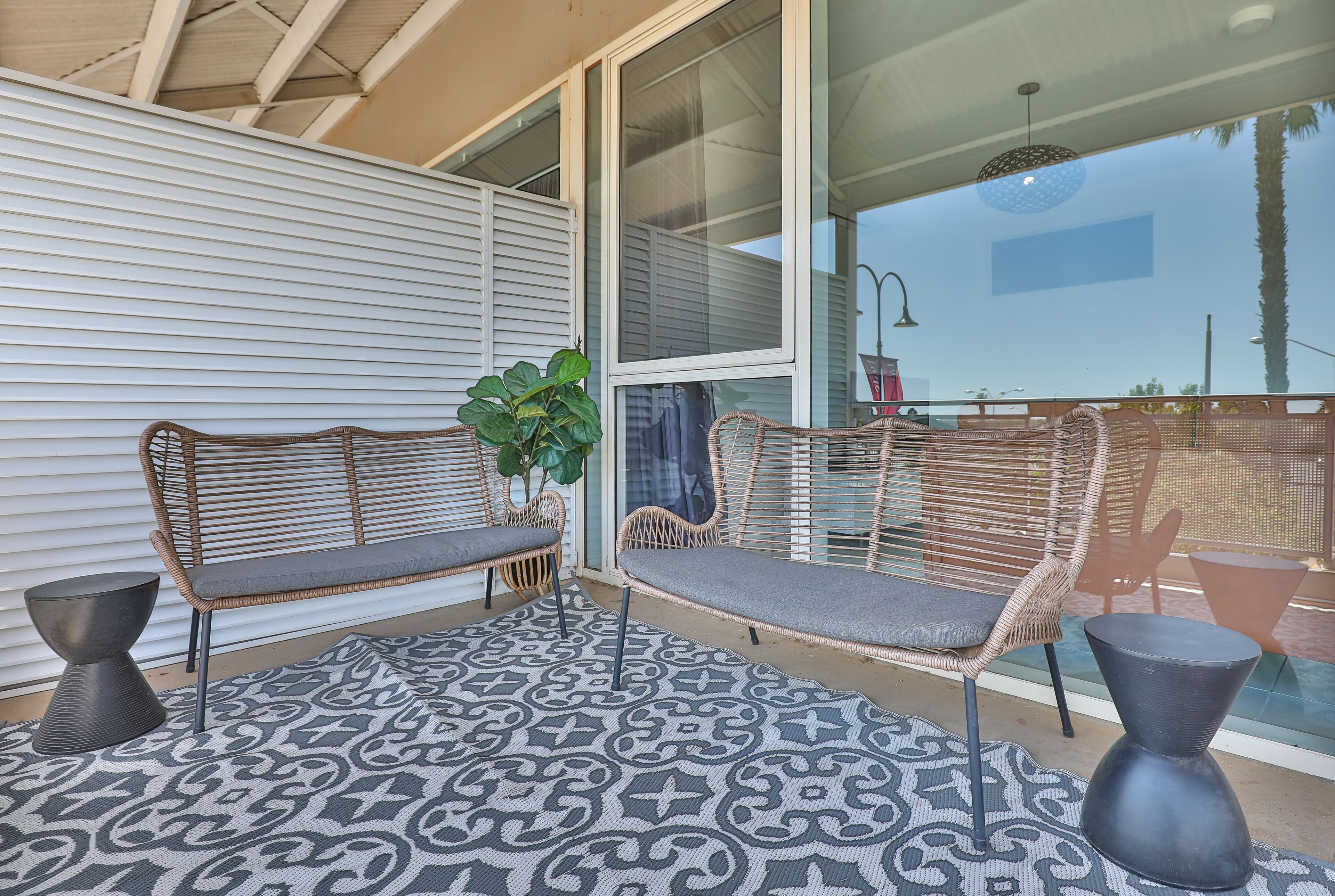 Un espace extérieur aménagé, abrité et doté de meubles en osier et d’un tapis à motifs.