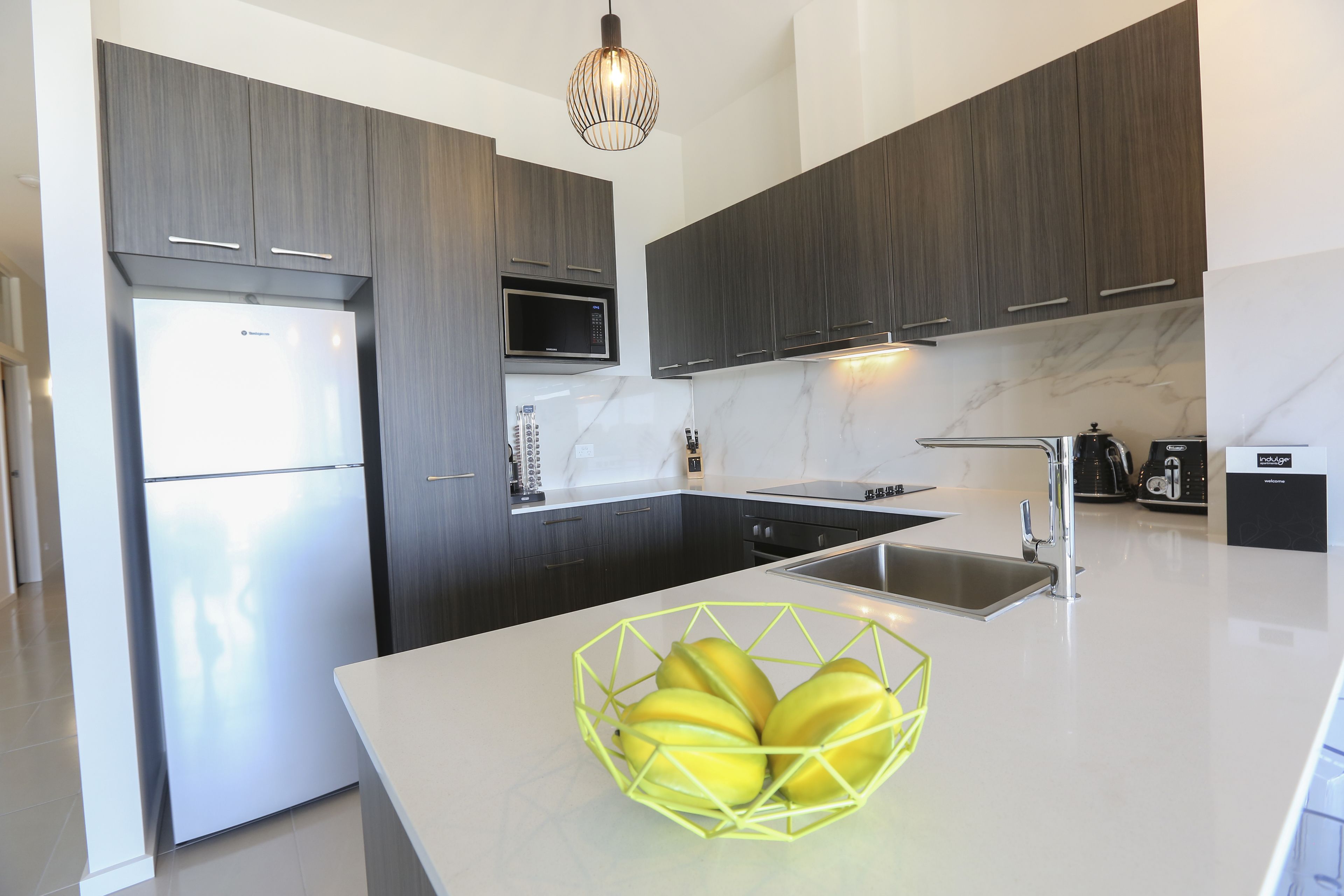 Een moderne keuken met donkerhouten kastjes, een roestvrijstalen koelkast, een magnetron en een spoelbak.