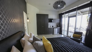 Una habitación de hotel moderna con una cama grande, kitchenette y un balcón con una silla.