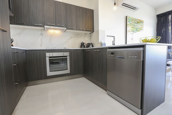 A modern kitchen with dark wood cabinets, a built-in oven, and a stainless steel dishwasher.