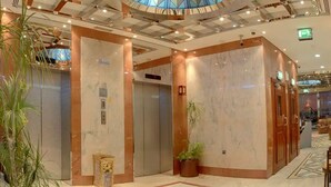 Een receptiehal met een centrale lift, marmeren wanden en een plafond met een glas-in-lood ontwerp.